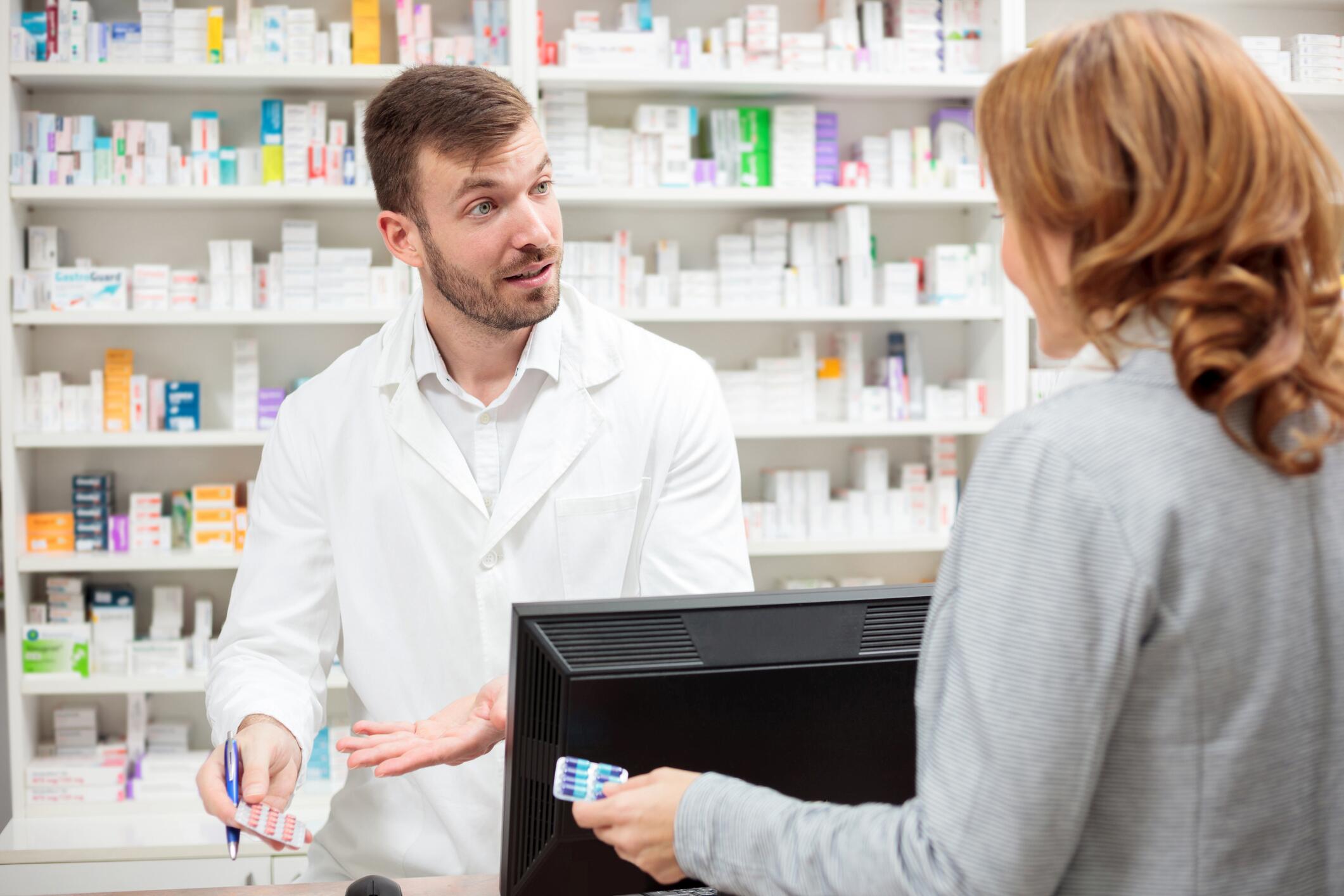 OG_YOUNG_MALE_PHARMACIST_STANDING_BEHIND_THE_COUNTER_CONSULTING_THE_FEMALE_PATIENT_ISTOCK_2023