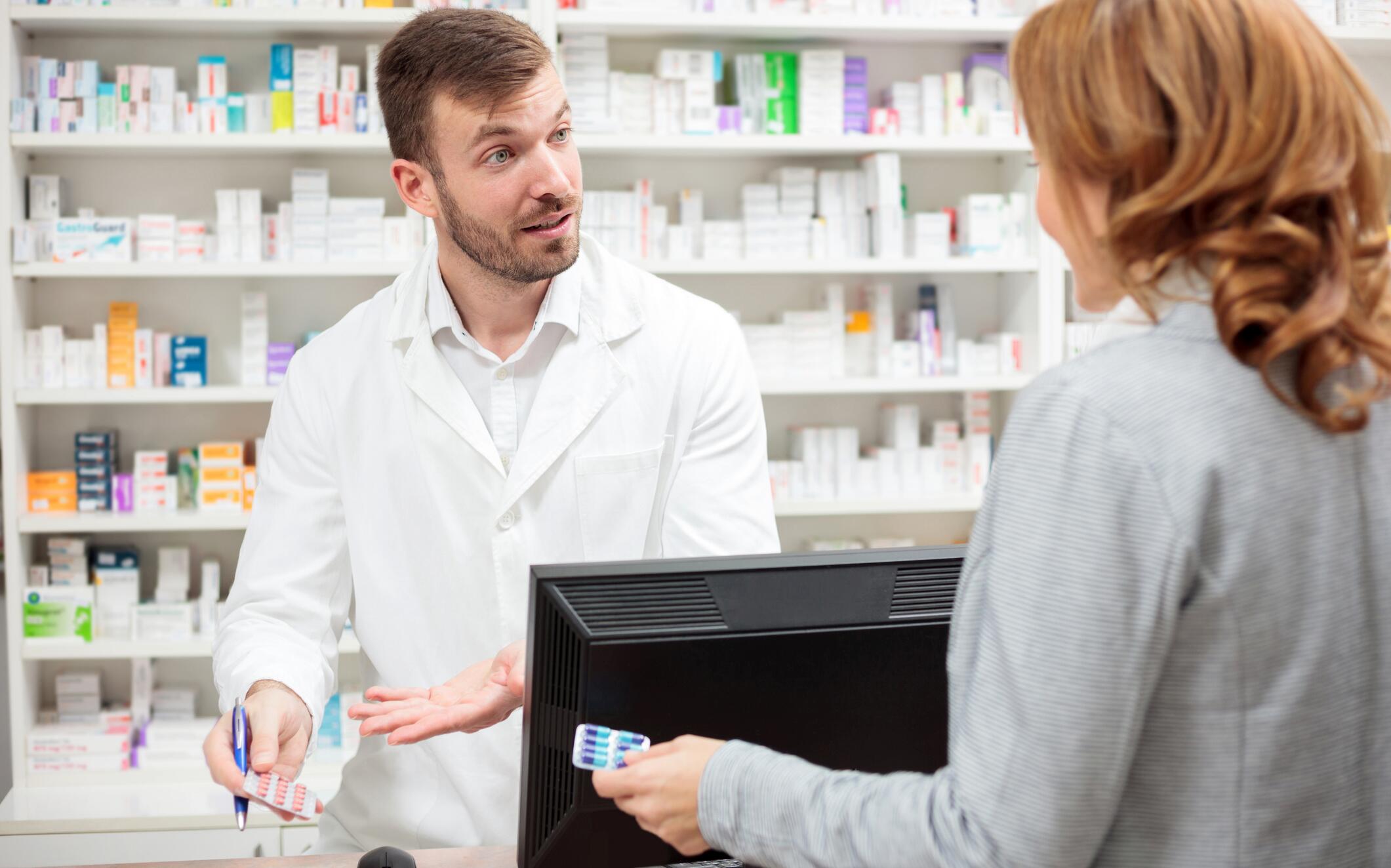 OG_YOUNG_MALE_PHARMACIST_STANDING_BEHIND_THE_COUNTER_CONSULTING_THE_FEMALE_PATIENT_ISTOCK_2023