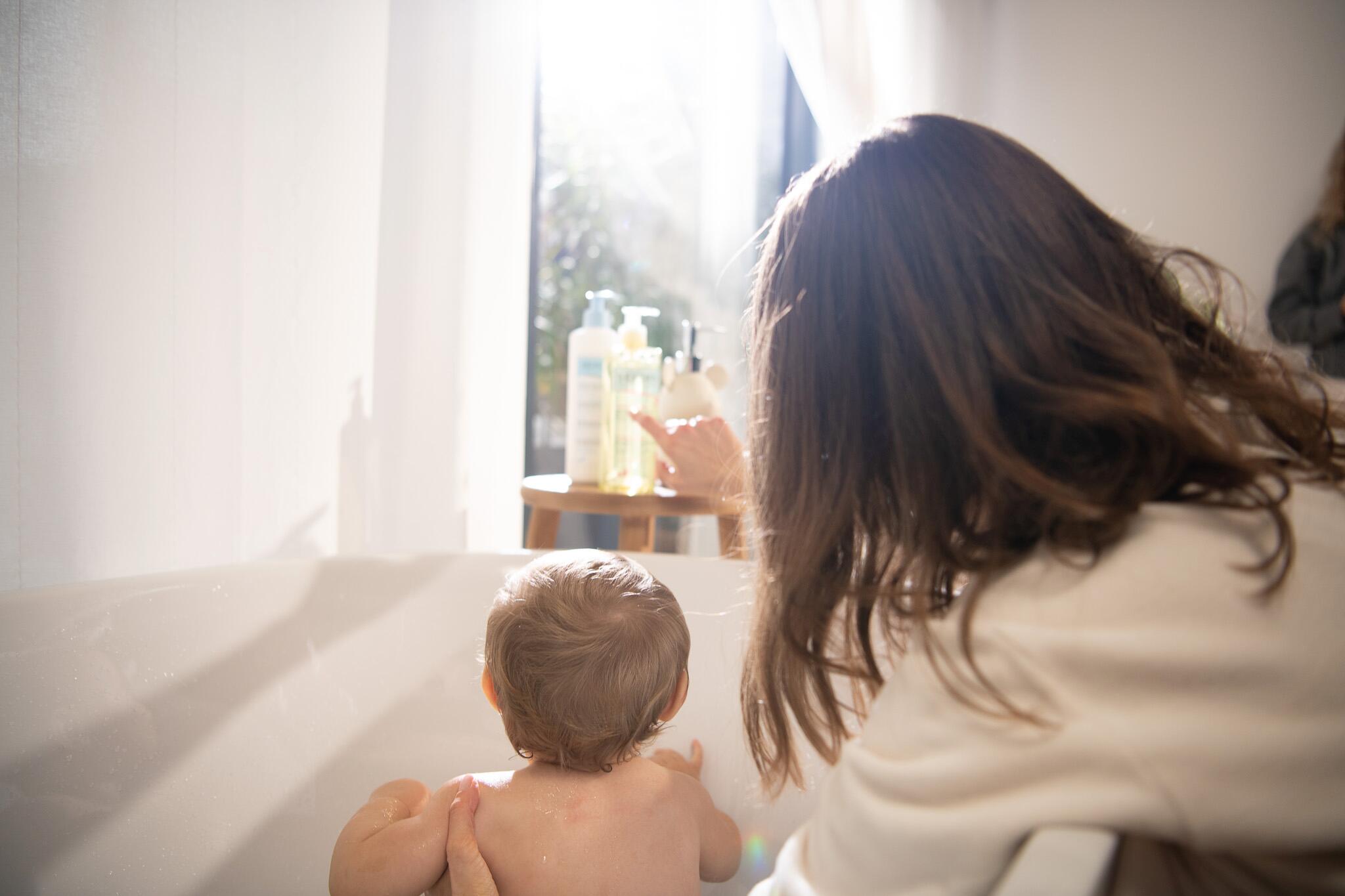 Mum and baby in the bath looking at the bottles of Dexeryl Emollient Cream and Cleansing Oil